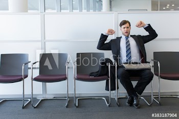 Tired young businessman yawning and stretching in office lobby
