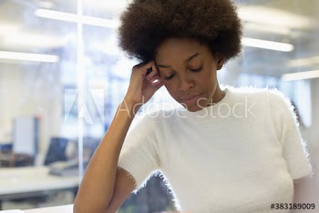 Tired young businesswoman with afro and eyes closed in office