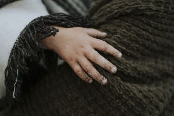 Toddler's Hand over Brown Knitted Garment