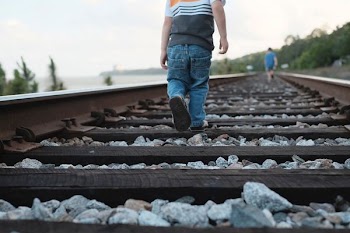toddler walking on train rail during daytime