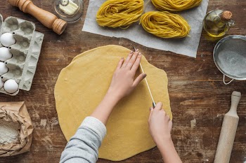 Top view of female hands cutting dough for pasta on wooden table