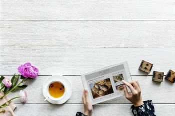 Top View of Person Using Tablet Computer Beside Teacup and Saucer With Brown Tea on Table Top