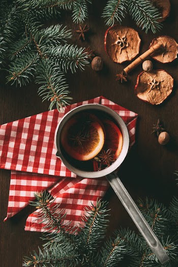 Top view of traditional christmas hot spiced wine on wooden background with dried apple slices and pine branches