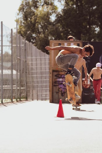 Topless Man Doing Tricks on a Skateboard Near People