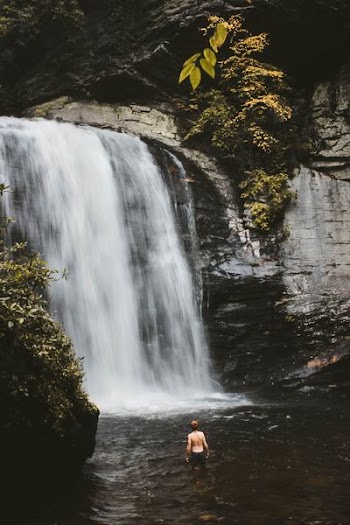 topless man in body of water in front of waterfalls