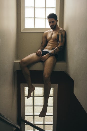 Topless Man Sitting Near White Painted Wall Posing for Photo