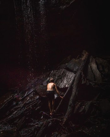 topless man standing at the bottom of waterfall