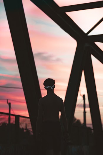 Topless Man Standing on Bridge during Sunset