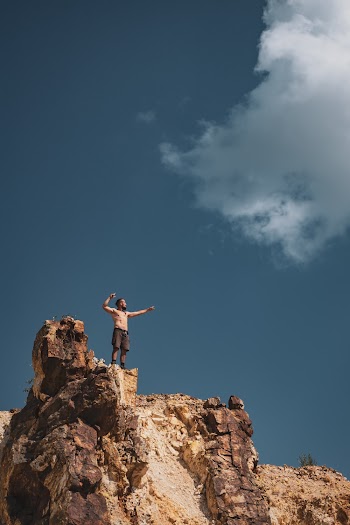 Topless Man Standing on Cliff