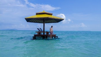 Topless Man Standing Under Gazebo Surrounded by Body of Water