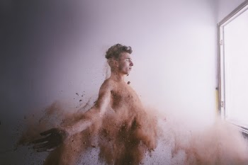 Topless Man Throw a Brown Powder in Front of Window in Room