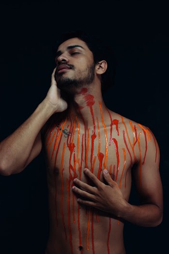 Topless Man With Multicolored Paint on His Body Standing While Putting Right Hand on His Face