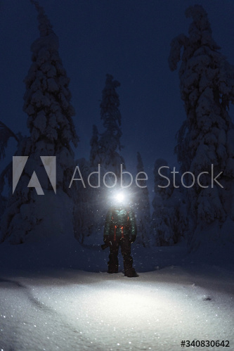 Trekker with a headlamp walking in a snowy Riisitunturi National Park, Finland