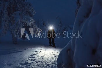 Trekker with a headlamp walking in a snowy Riisitunturi National Park, Finland