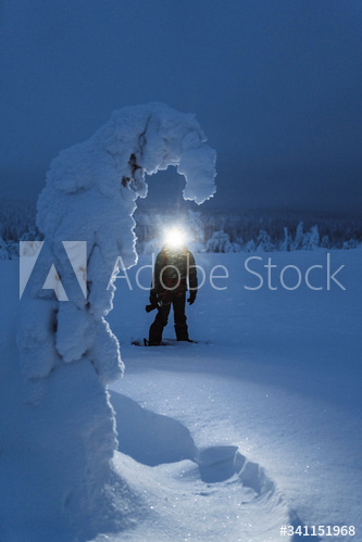 Trekker with a headlamp walking in a snowy Riisitunturi National Park, Finland
