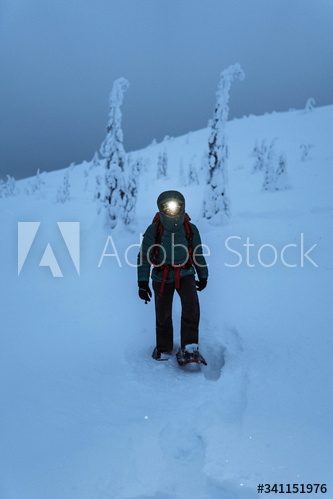 Trekker with a headlamp walking in a snowy Riisitunturi National Park, Finland