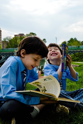 Two Boys Seated on the Grass Laughing and Reading Books