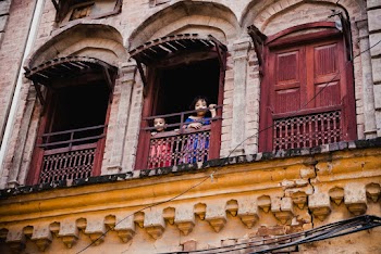 Two Children Standing on the Window of House