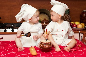 two little babies in the cook costumes at the kitchen sitting on the table