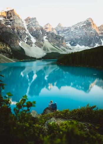 two man sitting on rock watching lake