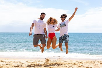 Two Men and One Woman Jumping Near Shore