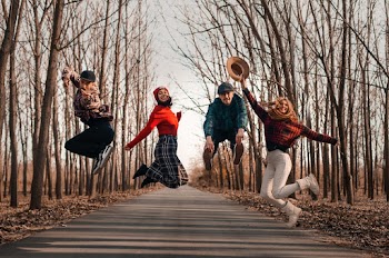 Two Men and Women Jumping on Roadway Surrounded by Bare Trees