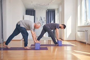 Two men performing a standing forward bend