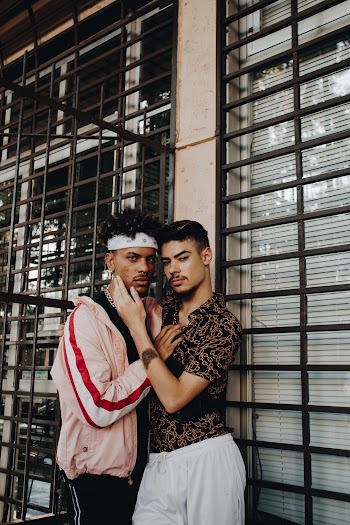 Two Men Posing Beside a Metal Grill While Holding Each Other