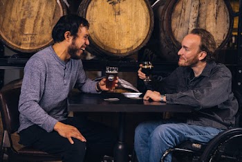 Two Men Sitting at the Table Holding Drinking Glasses While Smiling
