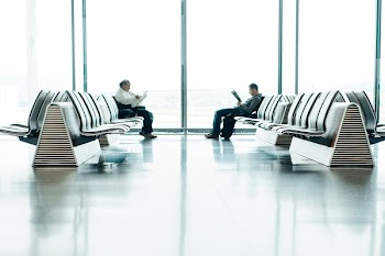 Two Men Sitting in Front of Each Other on White Gang Chairs in Airport Waiting Area