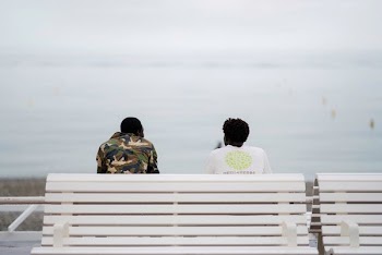 two men sitting on bench facing sea