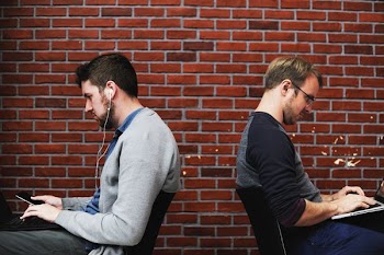two men sitting on black chairs towards red brick wall
