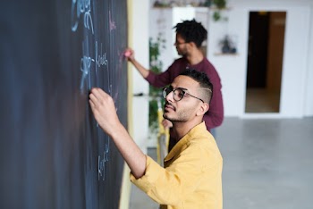 Two Men Writing on Chalkboard