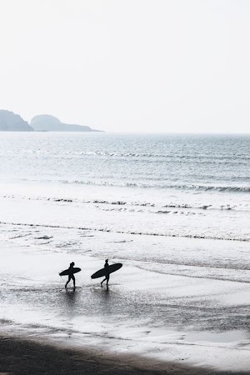 two people carrying surfboards at beach during daytime