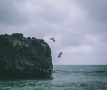 Two People Jumping on Body of Water