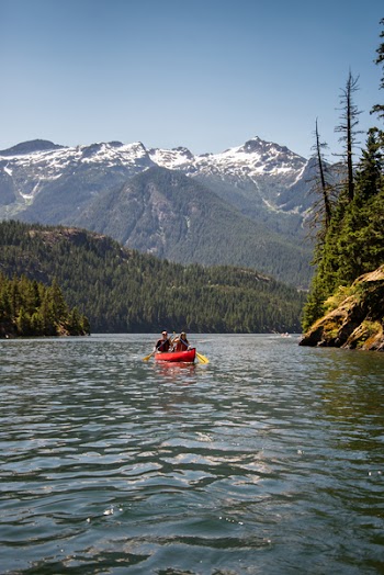 Two People on Red Kayak Floating on Body of Water Near Mountain Under Blue Sky