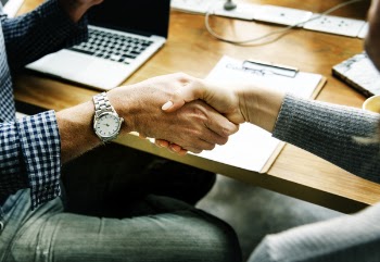 Two People Performing Handshake in Front of Table