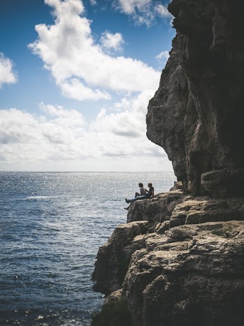 Two People Sitting By The Cliff