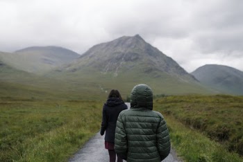 Two People Wearing Bubble Jackets While Walking on Pathway Between Green Grass