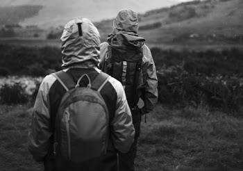 Two People With Backpacks Hiking on Green Field Greyscale Photography