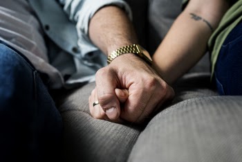 Two Person Holding Hands While Sitting on Grey Cushion