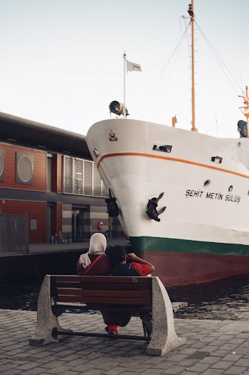 Two Person Sitting on Bench Facing Boat on Dock