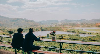 Two Person Sitting on Chair in Front of Lake and Mountains