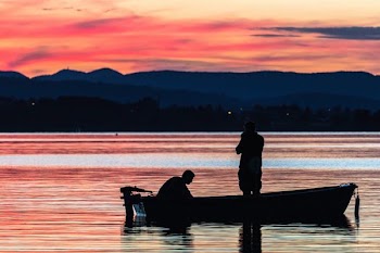 two person standing on boat on body of water during golden hour