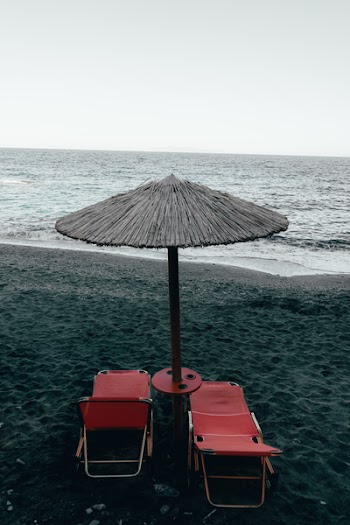 Two Red Pool Chairs Under Patio Umbrella Near Shore