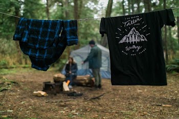 two shirts hanging near woman and man beside blue tent under tall trees