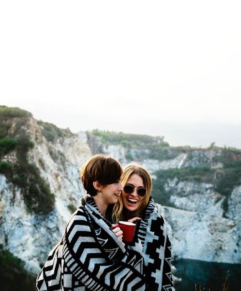 two woman covered by blanket holding cup of coffee near the mountain