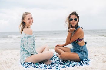 two woman sitting near each other near shoreline during daytime
