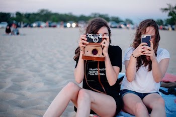 two woman taking photos using smartphone and camera