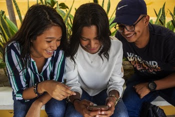 Two Women and a Man Smiling While Looking at a Phone